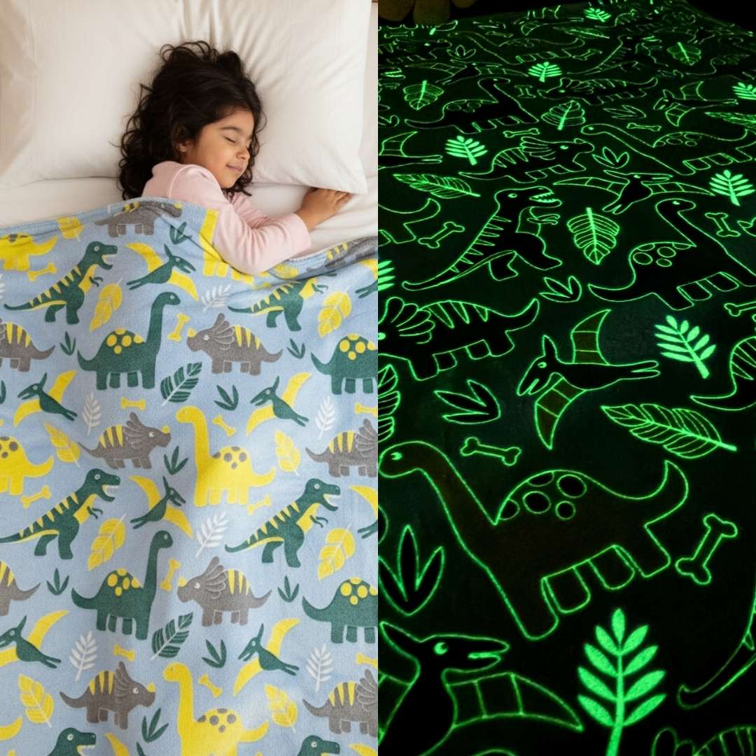 Girl sleeping under a light blue Famyo dinosaur-themed glow-in-the-dark blanket, shown glowing green with dinosaur and leaf patterns in the dark.
