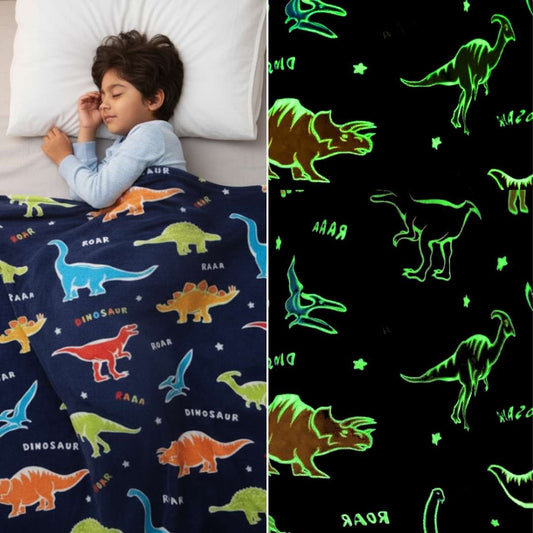 Child sleeping under a navy blue Famyo dinosaur-themed glow-in-the-dark blanket, shown glowing with green dinosaur outlines in the dark.