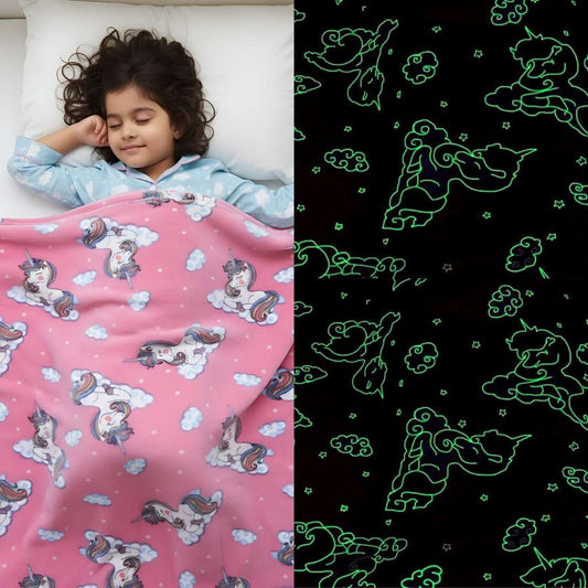 Girl sleeping under a pink Famyo glow-in-the-dark blanket with unicorn and cloud patterns, glowing green in the dark.