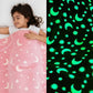 Girl sleeping under a pink Famyo glow-in-the-dark blanket with moon and star patterns, shown glowing green in the dark.